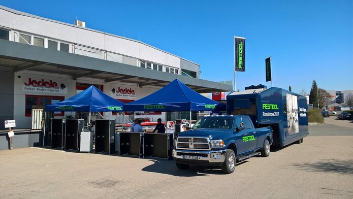 Gazebo per eventi 3x3m blu personalizzati con logo verde Festool abbinati a furgoncino e caravan aziendali davanti negozio di fai da te Jedele