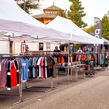 I gazebo promozionali bianche fungono come gazebo di vendita in occasione di un evento. Sotto i gazebo sono appese diverse magliette.