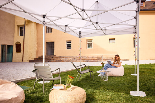 Gazebo Ecotent bianco 6x4m su gairdino davanti alla biblioteca di Bressanone utilizzato outdoor ripara dal sole una studentessa bionda che legge 