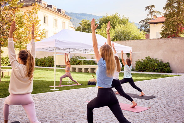 Il gazebo pieghevole bianco viene utilizzato per una lezione di yoga. L'istruttore di yoga è in piedi sotto di essa. Davanti al gazebo ci sono i partecipanti alla lezione di yoga.