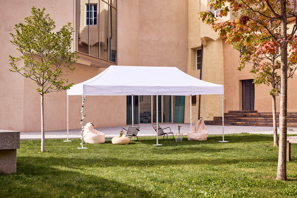 Gazebo Ecotent bianco 6x4m su gairdino davanti alla biblioteca di Bressanone utilizzato outdoor per area relax con puf, tavoli e libri