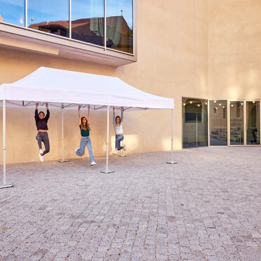 Tre ragazze si dondolano appese ad un gazebo pieghevole 6x4 m bianco Ecotent fissato al suolo con dei pesi per gazebo in ghisa a 20kg