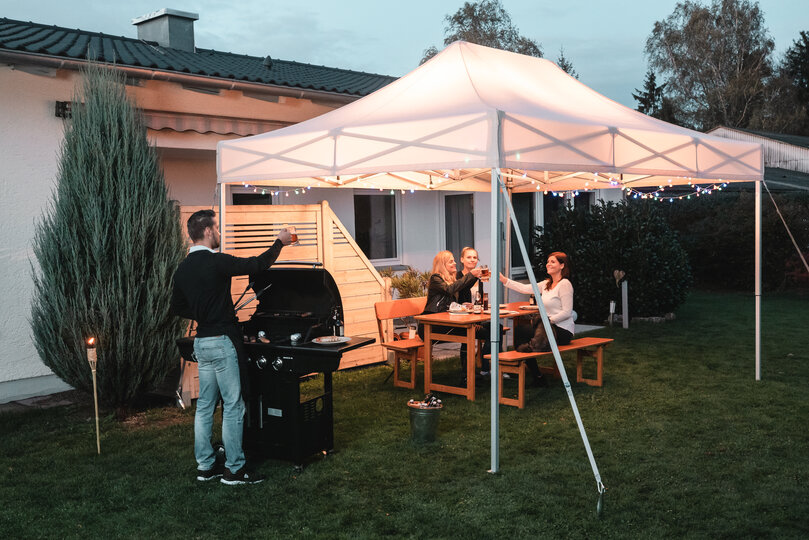 Gli amici festeggiano un barbecue e una festa in giardino sotto il gazebo da giardino. Il gazebo è decorato a festa con luci fiabesche.