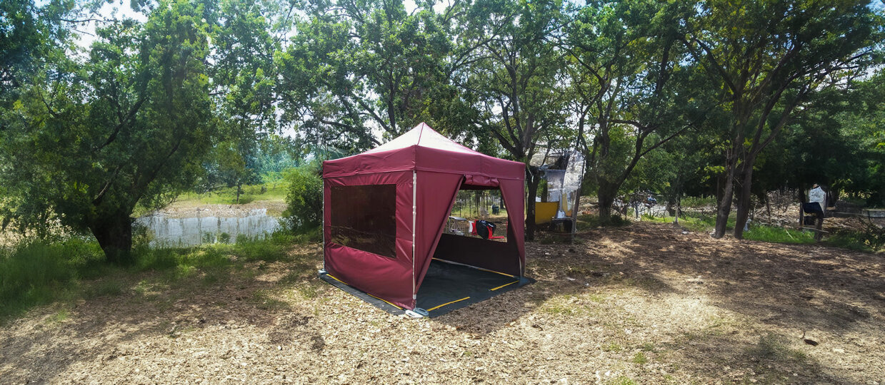 Gazebo pieghevole 3x3 da campeggio color bordeaux con teli laterali e pavimento in pvc in un camping