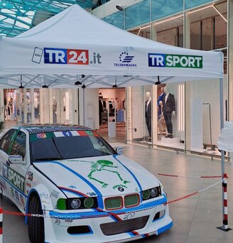 Gazebo pieghevole 4,5x3m bianco personalizzato con logo TR24 e TRSPORT serve da gazebo espositivo per un auto sportiva personalizzata nella hall di un centro commerciale